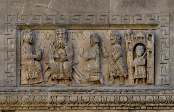 Fidenza, duomo (Cattedrale di San Donnino), facciata, sculture tra il portale sinistro e il portale maggiore:“Il Re Erode”.
La lastra raffigura Erode, re di Israele dal 37  fino al 4 a.C. – seduto su un faldistorio, in abiti e con le insegne regali medievali. 
Alla sua destra, seduta di profilo, una figura femminile (la regina?) che tiene nella mano sinistra un contenitore cilindrico. 
Alla sinistra del sovrano un nobiluomo inginocchiato presentato da un soldato armato di spada e vestito di elmo e giaco medievale. All’estrema destra sotto un edificio un uomo armato di spada e vestito d’una tunica ornata. Sulla lastra, a destra e sinistra della testa del re, è incisa l’iscrizione ERODES.
Non è improbabile che la scena rappresenti  il momento in cui il sovrano ordina la Strage degli innocenti (Mt 2,16-18), che si collegherebbe coerentemente con l’Adorazione dei Magi, il Sogno di Giuseppe e la Fuga dei tre re, raffigurati in altri bassorilievi della facciata.
Opera di Benedetto Antel...