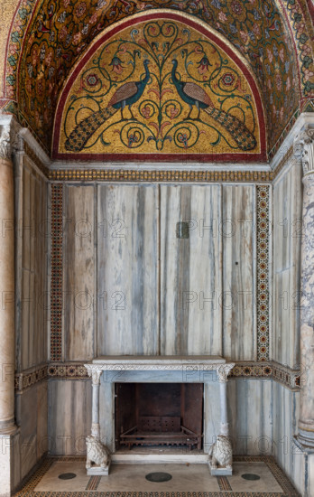 Palermo, Palazzo Reale o Palazzo dei Normanni, Torre Pisana, Sala di Re Ruggero: veduta della sala voluta da Re Ruggero II d'Altavilla. E' caratterizzata da ampie superfici a mosaico di grande pregio raffiguranti elementi vegetali (palme e banani) e scene di carattere aulico e venatorio, simboli del potere normanno (battute di caccia con arcieri e cervi, rappresentati pavoni, cigni, oltre i mitologici centauri, grifi e altri animali esotici tra cui leopardi e tigri fra lussureggiante vegetazione). I mosaici sono di stile greco - bizantino (secolo XIII).
Particolare di nicchia con caminetto con due leoni stilofori che reggono la mensola, lunetta con mosaico di pavoni; ricchi rivestimenti in marmo e colonnine angolari.

[ENG]
Palermo, The Royal Palace or Palazzo dei Normanni (Palace of the Normans), Pisana Tower,  the King Roger Room: view of the Room which was commissioned by King Roger II d'Altavilla. It is characterized by large mosaic surfaces of great value representing plant el...