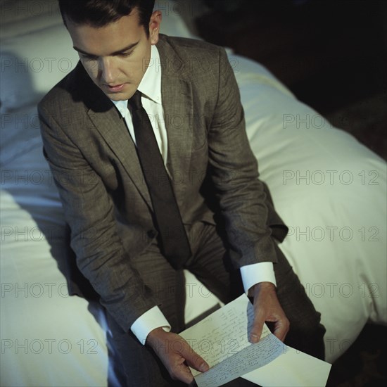 Man Sitting on Bed Reading Letter