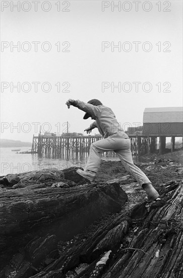 Boy Jumping on Rocks Along Shore, Rear View