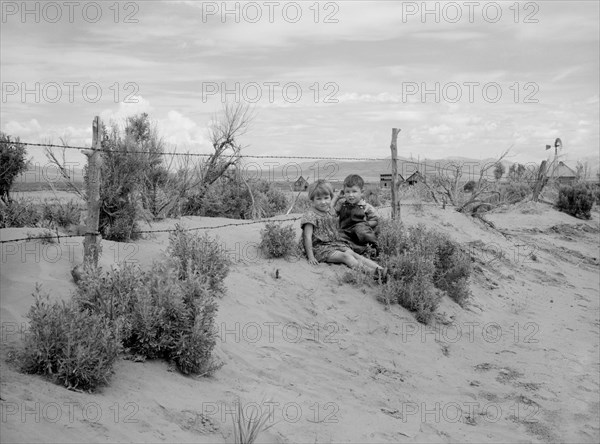 Two Children Sitting on Sandy Soil Blown Against Fence, Oneida County, Idaho, USA, Arthur Rothstein for Farm Security Administration (FSA), May 1936