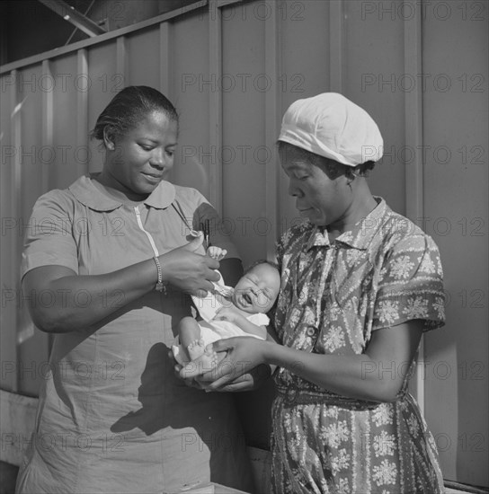 Nurse Examining Infant with Mother and Child Receiving Prenatal and Postnatal Care, Okeechobee Migratory Labor Camp, Belle Glade, Florida, USA, Marion Post Wolcott for Farm Security Administration, June 1940