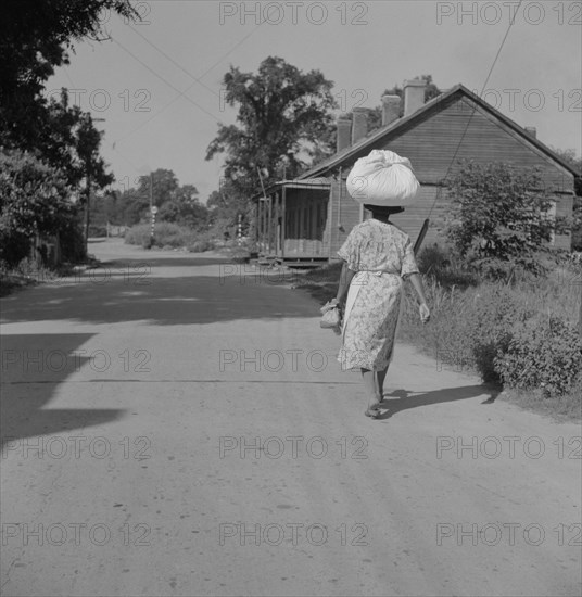 Woman Carrying Sack of Laundry on her Head along Dirt Road, Rear View, Natchez, Mississippi, USA, Marion Post Wolcott for Farm Security Administration, August 1940