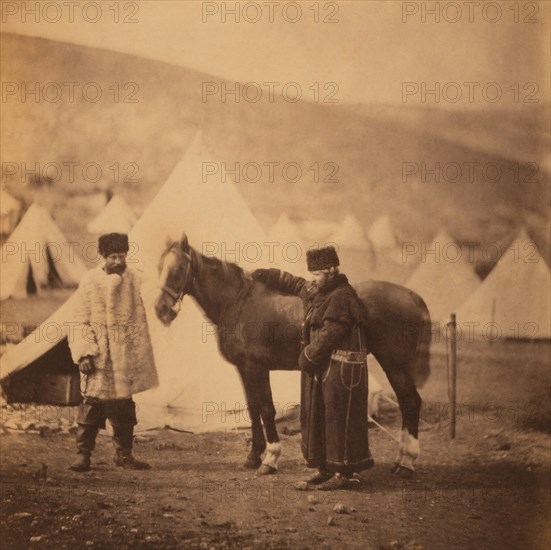 British Colonel Alexander Low, 4th Light Dragoons, Full-Length Standing Portrait in Winter Uniform with Servant and Horse, Military Tents in Background, Crimean War, Crimea, Ukraine, by Roger Fenton, 1855