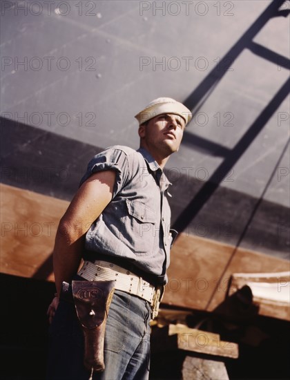 Coast Guard Sentry Standing Watch over New Torpedo Boat Under Constructions at Shipyard, Higgins Industries, Inc., New Orleans, Louisiana, USA, Howard R. Hollem for Office of War Information, July 1942
