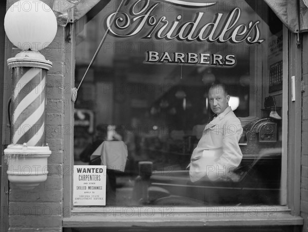 Portrait of Barber in Barber Shop Window, Help Wanted Sign Looking for Skilled Labor Resources Posted in Window by Virginia State Employment Service, Friddle's Barbers, Harrisonburg, Virginia, USA, John Vachon for Office for Emergency Management, May 1941