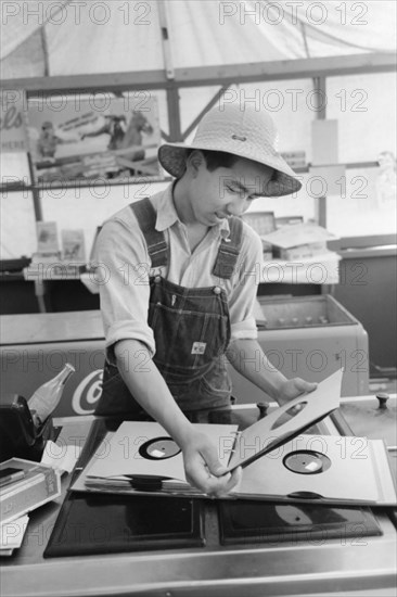 Japanese-American Farm Worker from the Farm Security Administration (FSA) Mobile Camp Selecting a Gramophone Record in Recreation Tent, Nyssa, Oregon, USA, Russell Lee, Farm Security Administration, July 1942