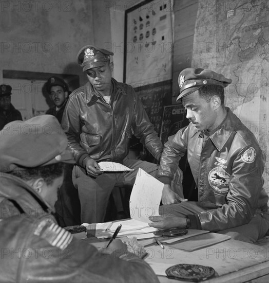 Tuskegee Airmen attending Briefing at Air Base, Woodrow W. Crockett, standing at center, Edward C. Gleed, Lawrence, KS, Class 42-K, Group Operations Officer, Seated on Right, and Unidentified Airman Seated on Left, Ramitelli, Italy, Toni Frissell, March 1945
