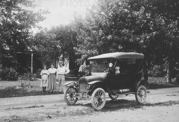 Family Standing on Sidewalk Next to Model T Automobile With Dog in Car