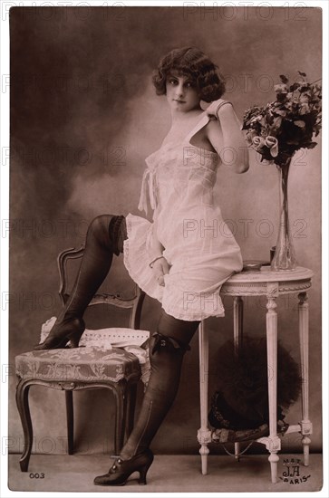 French Lingerie Model Leaning on Table With One Leg Raised on Chair, 1920