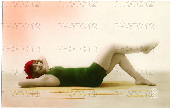 Smiling Woman in Green Swimsuit and Red Swim Cap Laying Down while Holding Parasol, Portrait, Hand-Colored French Postcard, circa early 1900's