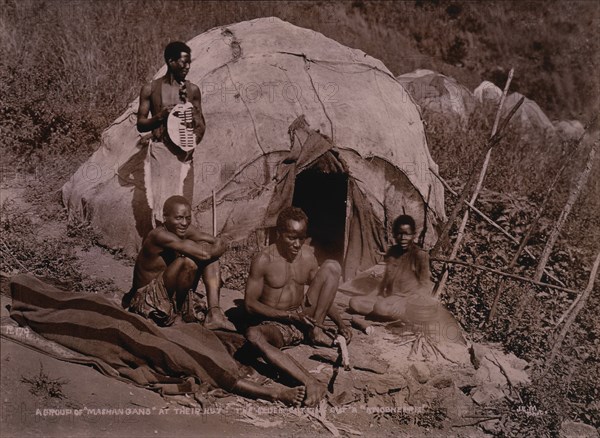 Group of Zulus in Front of Hut, Elder Zulu Cutting Knobkerrie, Africa, circa 1890
