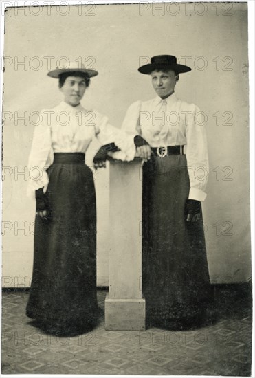 Portrait of Two Adult Women in Hats and Long Dresses Leaning on Pillar, circa 1870