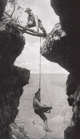 Photographer, Emery or Elsworth Kolb, Suspended on Climber's Rope in Crevasse and Photographing Canyon Wall as Another Man Straddles Cliff Opening while Holding the Rope, Grand Canyon, Arizona, USA, by Kolb Brothers, 1908
