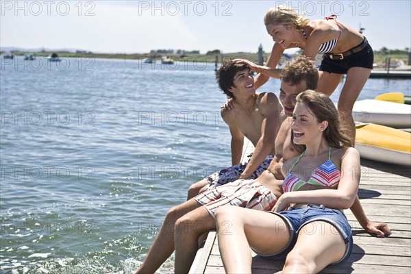 Two Young Couples Sitting on Edge of Pier Having Fun