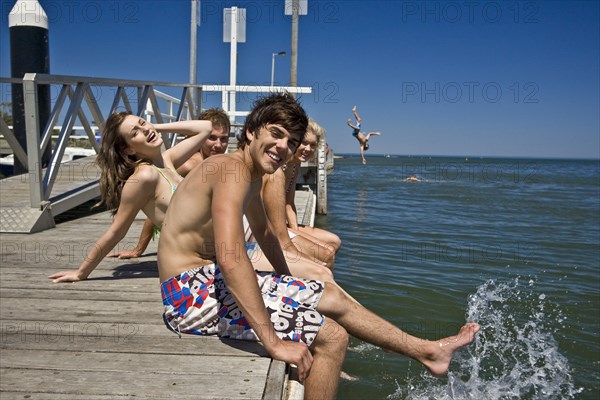 Two Smiling Young Couples Sitting on Edge of Pier