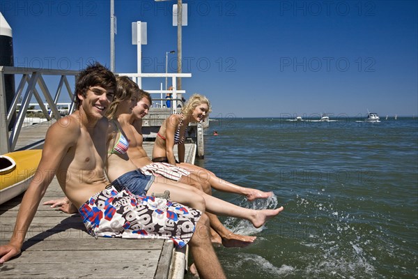 Two Smiling Young Couples Sitting on Edge of Pier