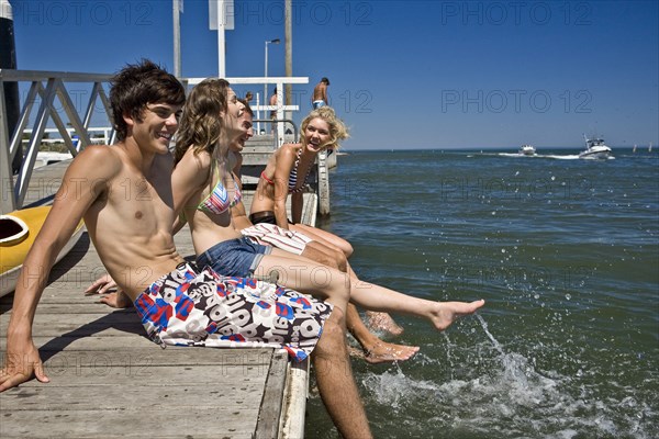 Two Smiling Young Couples Sitting on Edge of Pier