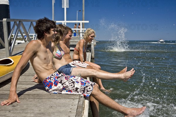 Two Smiling Young Couples Sitting on Edge of Pier