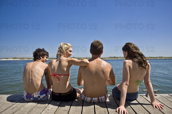 Two Young Couples Sitting on Edge of Pier, Rear View