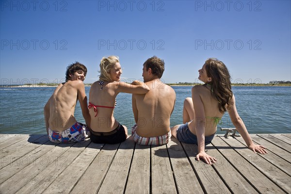 Two Young Couples Sitting on Edge of Pier, Rear View