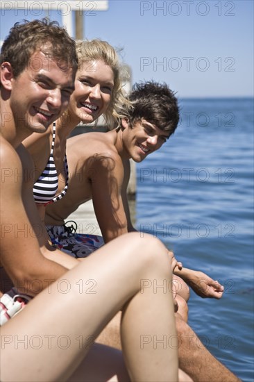 Three Smiling Young Adults Sitting on Edge of Pier