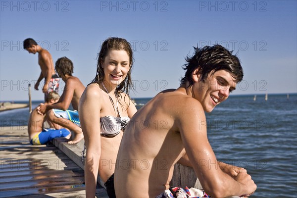 Smiling Young Couple Sitting on Edge of Pier