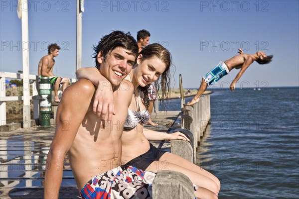 Smiling Young Couple Sitting on Edge of Pier