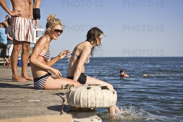 Two Young Women Sitting on Edge of Pier