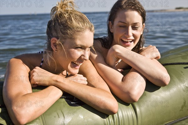 Two Smiling Young Women in Water Resting on Side of Dinghy