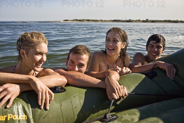 Two Smiling Young Couples in Water Resting on Side of Dinghy