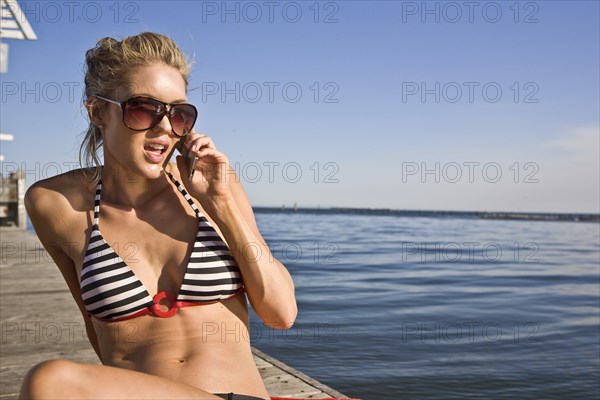 Young Woman Sunbathing and Talking on Cell Phone on Pier
