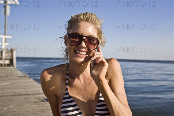 Smiling Young Woman Sunbathing and Talking on Cell Phone on Pier