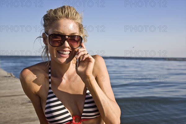 Smiling Young Woman Sunbathing and Talking on Cell Phone on Pier