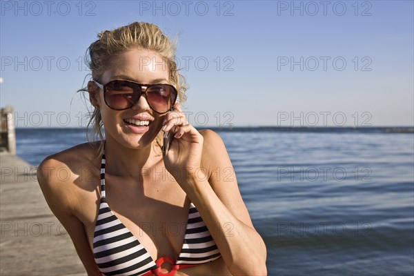 Smiling Young Woman Sunbathing and Talking on Cell Phone on Pier