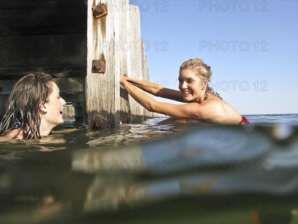 Two Young Women in Water With One Holding onto Pier Steps