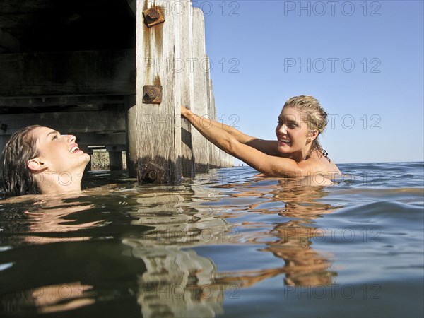 Two Young Women in Water With One Holding onto Pier Steps