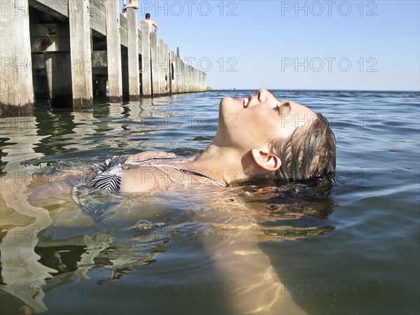 Young Woman Floating in Water Near Pier