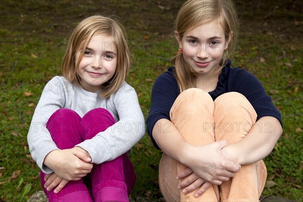 Two Smiling Girls With Arms Wrapped Around Legs