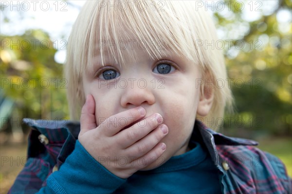 Young Blonde Boy With Hand Over Mouth
