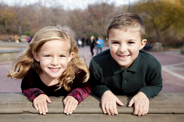 Smiling Boy and Girl Holding onto Ledge in Park