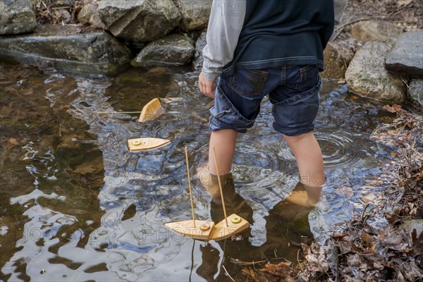 Child Playing with Toy Boats in Pond