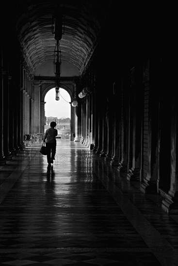Silhouette of Woman Walking Down Darkened Walkway Toward Sunlight, Venice, Italy