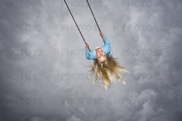 Girl On Swing against Grey Cloudy Sky