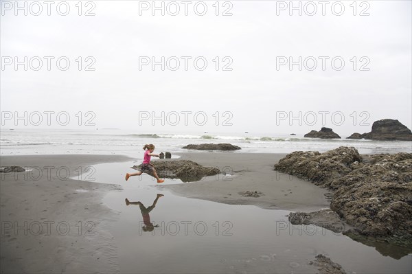 Girl Jumping Over Tidal Pool on Beach