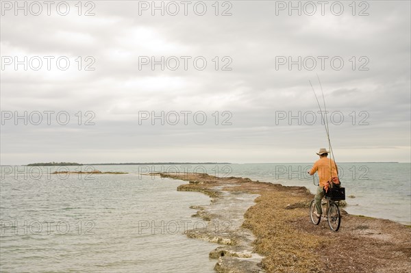 Man Riding Bicycle With Fishing Rods on Beach, Florida Keys, USA