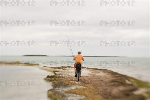 Man Riding Bicycle With Fishing Rods on Beach, Florida Keys, USA