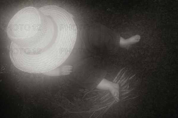 Young Boy in Large Hat Sitting on Ground with Carrots, High Angle View