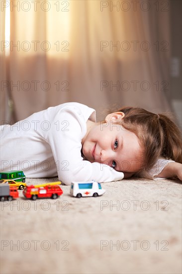 Smiling Girl Portrait on Floor with Toy Cars and Trucks