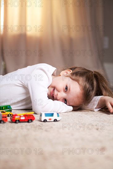 Smiling Girl Portrait on Floor with Toy Cars and Trucks